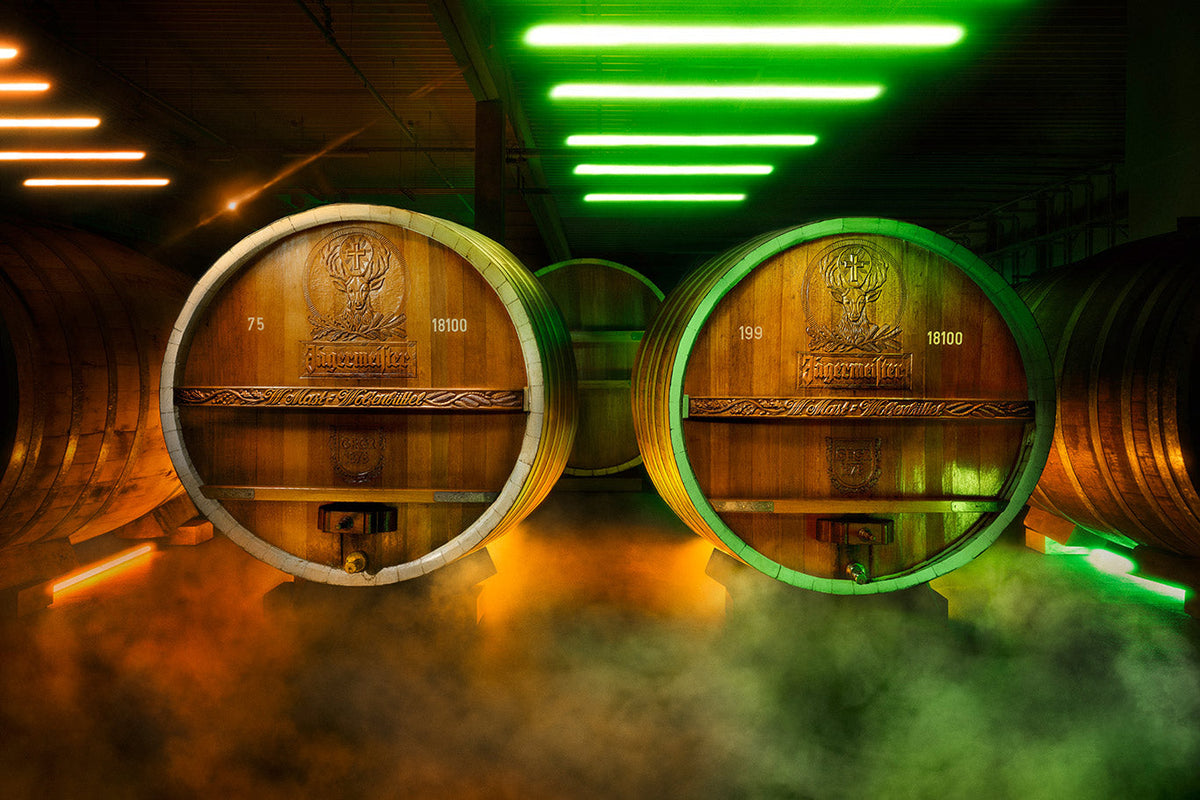 Two large wooden barrels with Jägermeister engraved at the front in a dim, orange and green lighted room