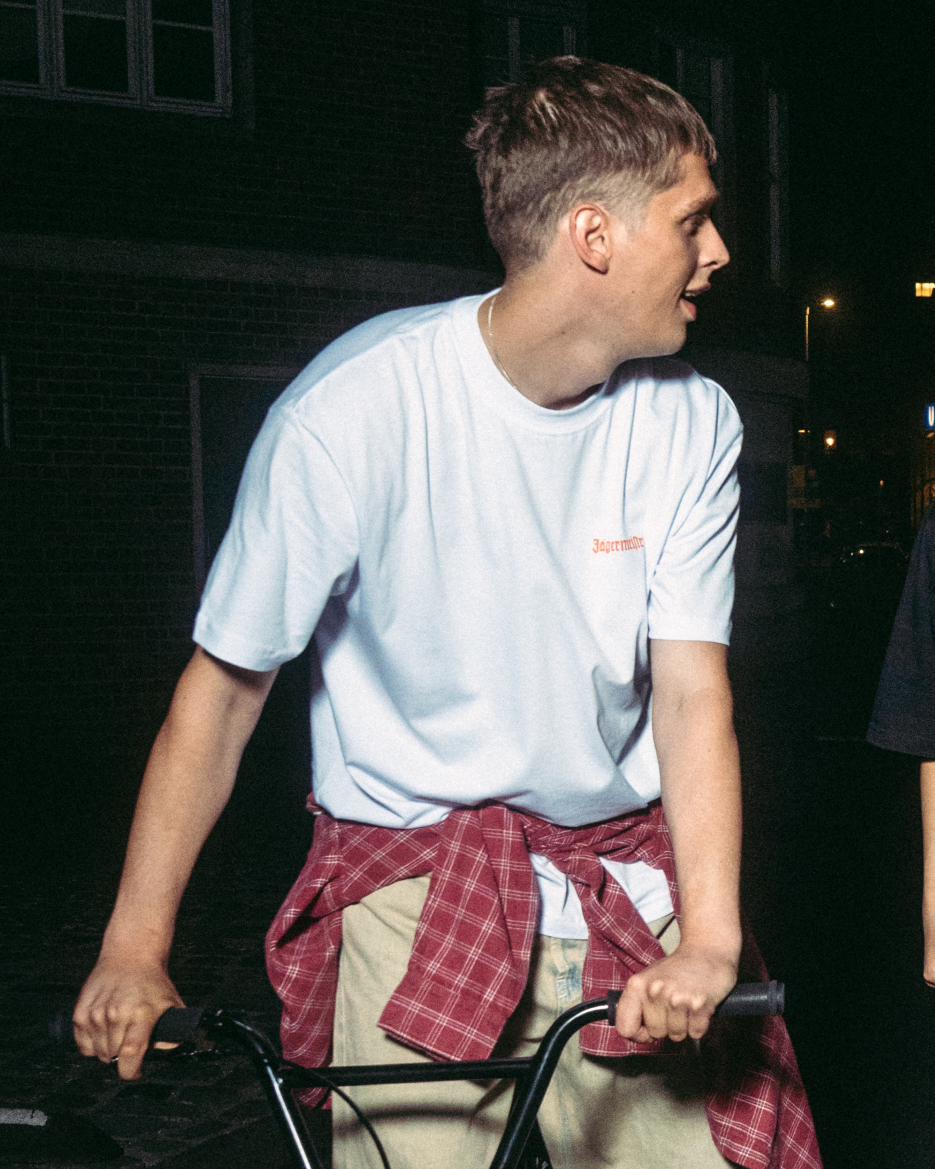 Person riding a bicycle at night, wearing a white Jägermeister T-shirt with a small logo on the chest.