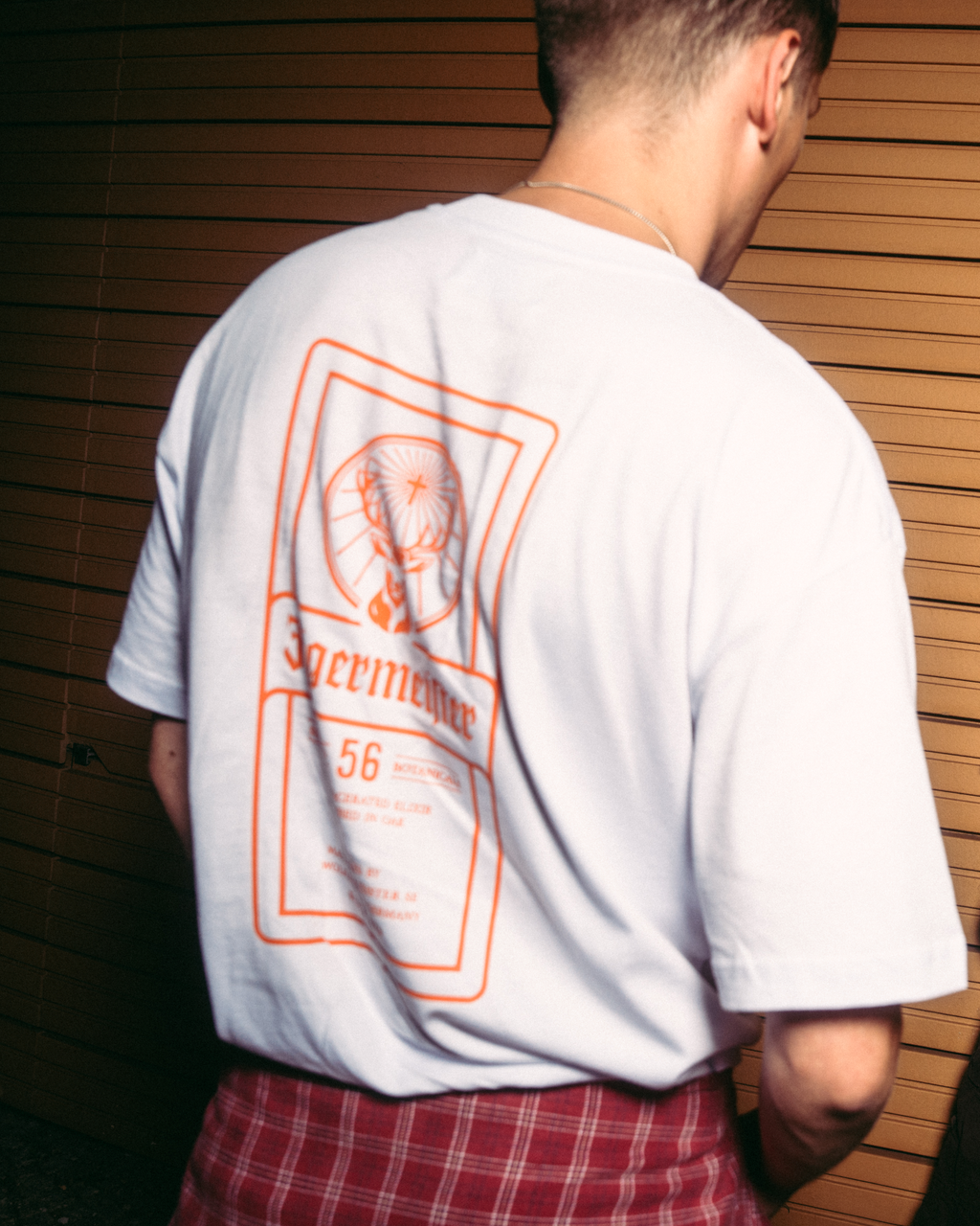 Vedere din spate a unui tricou alb Jägermeister, cu un imprimeu grafic mare inspirat de eticheta Jägermeister.