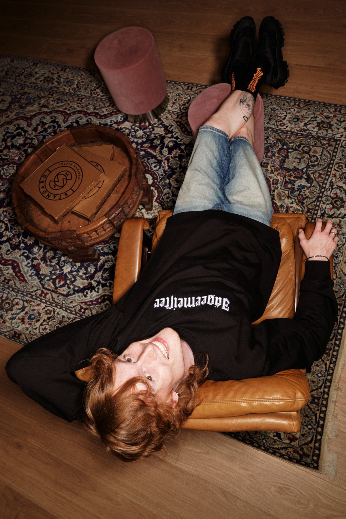 Person lying on a leather chair with feet up on a rug, wearing a black Jägermeister crewneck.