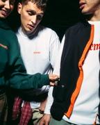 Trei tineri stând aproape unii de alții într-un decor întunecat, purtând articole vestimentare Jägermeister. Unul poartă un hanorac verde închis, altul poartă un tricou alb cu mânecă lungă, iar al treilea poartă o jachetă neagră și portocalie cu fermoar peste un tricou alb.