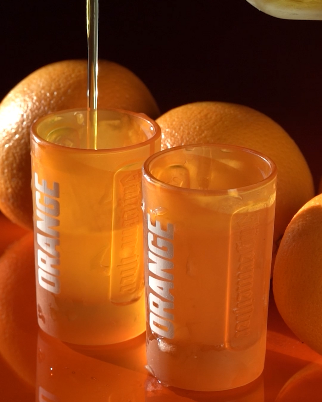 Două pahare de shot Jägermeister portocalii, cu portocale în fundal.
