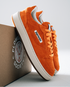 Orange Jägermeister sneakers with white soles and a white side label reading 'Jägermeister', displayed with a brown box printed with 'Flower Society' on a light gray background.