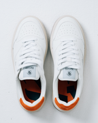 A pair of white Jägermeister sneakers shown from a top-down view on a light gray background. The shoes feature white laces, a white leather upper, and a bright orange heel accent.